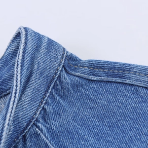 Detailansicht der Denim-Textur und der gelben Doppelnadel-Nähte am Ausschnitt des Hemdes