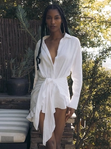 Detail of white long sleeve linen shirt dress with waist tie and irregular hemline