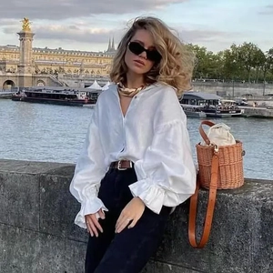 Street style shot of white bubble sleeve linen shirt paired with a straw bucket bag