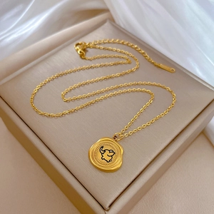 Detailed view of a gold elephant pendant necklace on beige jewelry display with silk