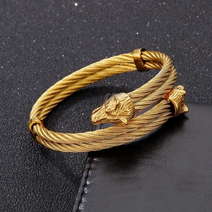 Macro detail of golden wolf head terminal and dual braided cable on stainless steel bangle