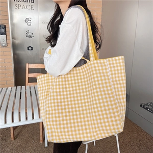 Close-up of yellow and white checkered canvas tote bag worn by a model in a cafe setting