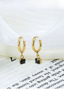 Detail view of gold titanium earrings with black faceted gemstone on white ribbon