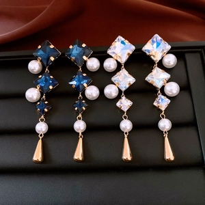 Macro shot of long geometric drop earrings with crystals and pearls on a black tray