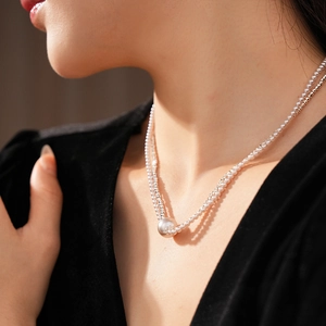 Detail of double-layer pearl necklace featuring a large round pearl pendant on a model
