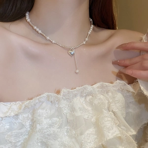 Detail of a pearl heart pendant necklace worn by a model in warm indoor lighting