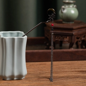Detail of a crescent moon hair stick with red beads and tassels in a vintage vase