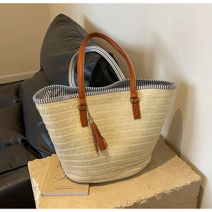 Detailed close-up of woven straw tote bag with brown PU leather handles and tassel accent