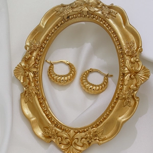 Detail shot of golden croissant earrings on white silk inside a vintage gold frame