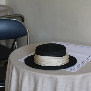 Classic black flat top wide brim straw hat with champagne silk ribbon on table