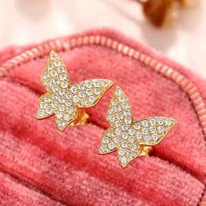 Macro shot of gold butterfly stud earrings with micro-pave cubic zirconia on pink velvet