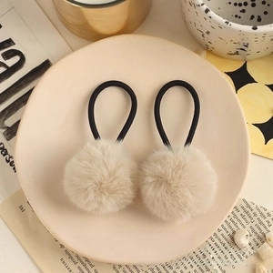 Detail of cream plush pom pom hair ties on a ceramic plate with soft French decor