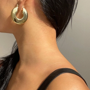 Close-up of chunky gold hollow hoop earring worn by a model with polished finish