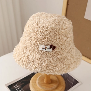 Detailed close-up of a beige faux shearling bucket hat with a cute bow and tag decoration