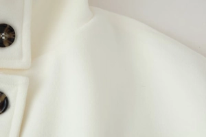 Close-up of white wool coat collar with large dark tortoiseshell buttons and texture