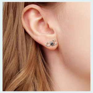 Macro shot of a silver scorpion earring with a pear-cut iridescent stone on the ear lobe