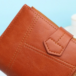 Close-up detail van bruine PU lederen korte damesportemonnee met nette stiksels en rits.