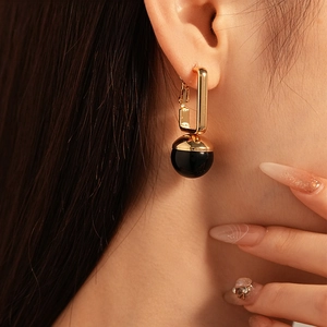 Vintage gold rectangular geometric earrings with black circular resin charms on a model