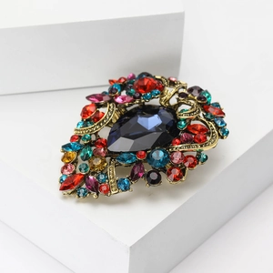 Macro shot of vintage gold alloy brooch with deep blue pear-shaped gem and colorful rhinestones