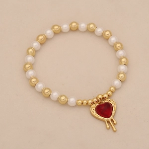 Detail view of a gold and white pearl beaded bracelet with a red melting heart charm