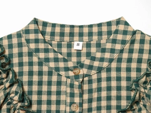Detail of green and khaki plaid shirt featuring a round neckline and ruffled edges