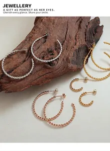 Detailed view of twisted gold silver and rose gold hoop earrings on natural wood stand