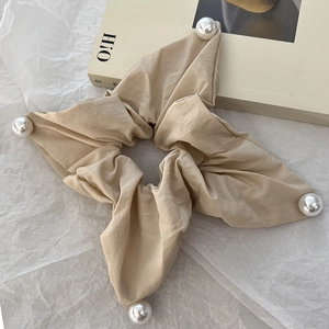 Detailed view of beige fabric square scrunchie with large white pearls on a paper background