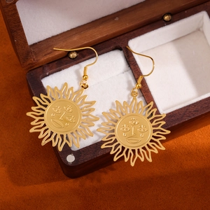 Golden sunface drop earrings with hollow cutouts resting on a wooden jewelry box