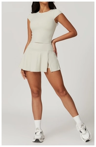 Dettaglio della gonna a pieghe a vita alta e del crop top coordinato color crema