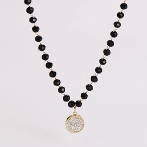 Detail of black faceted bead chain with a gold circular pendant encrusted with crystals