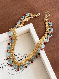 Détail du collier de perles artisanal avec des perles dorées, bleues et rouges en vagues