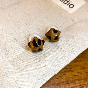 Macro view of star-shaped leopard print earrings with elegant pearl backings on wood