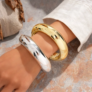 Pair of thick polished geometric round bangles in gold and silver finish on hand