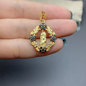 Macro shot of gold Virgin Mary pendant with black zircon stones held by fingers