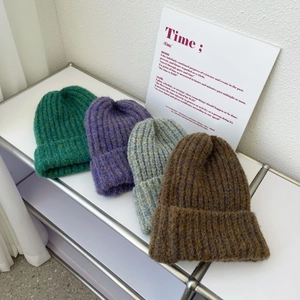 Detail of chunky knit beanies in green, purple, blue, and brown on a minimalist rack