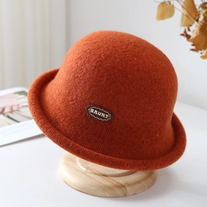 Close-up of rust orange felt bucket hat featuring an oval brown lettered leather patch