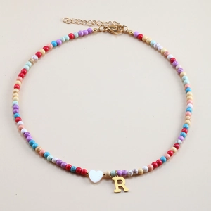 Colorful beaded necklace with gold letter R and white heart pendant on a neutral background