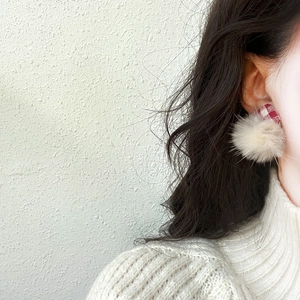 Sweet cream-colored pom pom earrings with red plaid fabric accents worn by a model