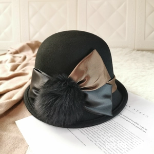 Detail view of black wool felt hat featuring a decorative metallic bow and fur pom-pom