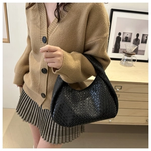 Detailed view of black woven textured underarm hobo bag held by a model in a room