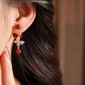 Close-up of butterfly pearl drop earrings with red beads and crystals worn by a model