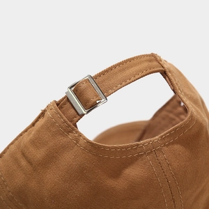 Detail of adjustable silver metal buckle and stitching on caramel cotton baseball cap