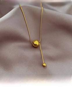 Detail of gold ball pendant necklace with sleek metal bar on elegant silk background
