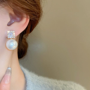 Close-up of elegant gold earrings with square cubic zirconia and white pearls on model