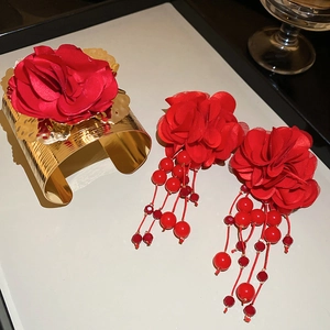 Detail of gold metal cuff bracelet and red fabric flower earrings with beaded tassels