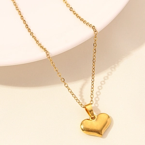 Close-up of a polished heart-shaped gold pendant on a delicate chain with a textured backdrop