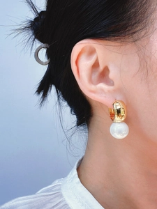 Close-up of a wide gold hoop earring with a large white pearl on a female model