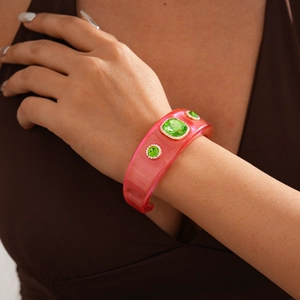 Close-up of pink resin bangle with three green faceted stones worn on a wrist