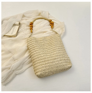 Detail of rainbow straw bucket bag with wooden bead handle on white dress and book