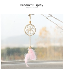 Detail of handmade dreamcatcher with pink feathers and wooden beads hanging on a branch.